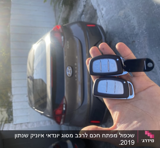 שני מפתחות רכב חכמים ביד מול רכב חונה